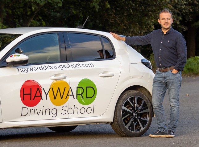 Andy Hayward, driving instructor, standing next to his driving school car.