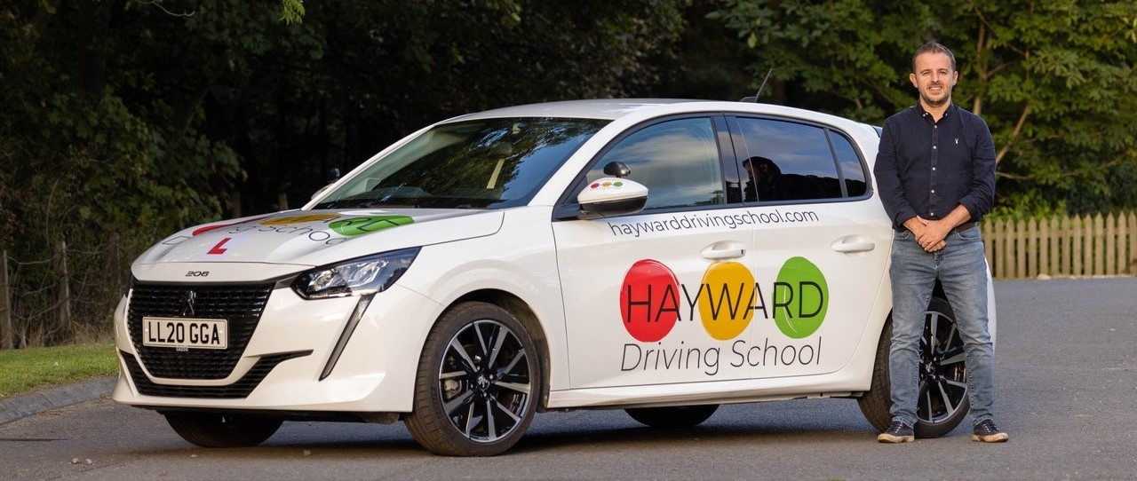 Andy Hayward, driving instructor, standing next to his driving school car.